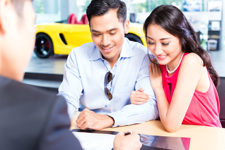 Asian Couple signing sales contract for car at dealership